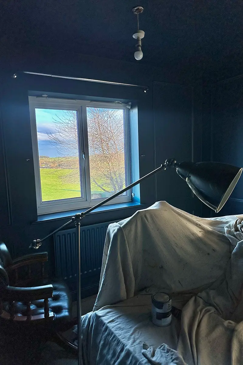 A freshly decorated room with dark blue walls. The furniture is still covered with dust sheets