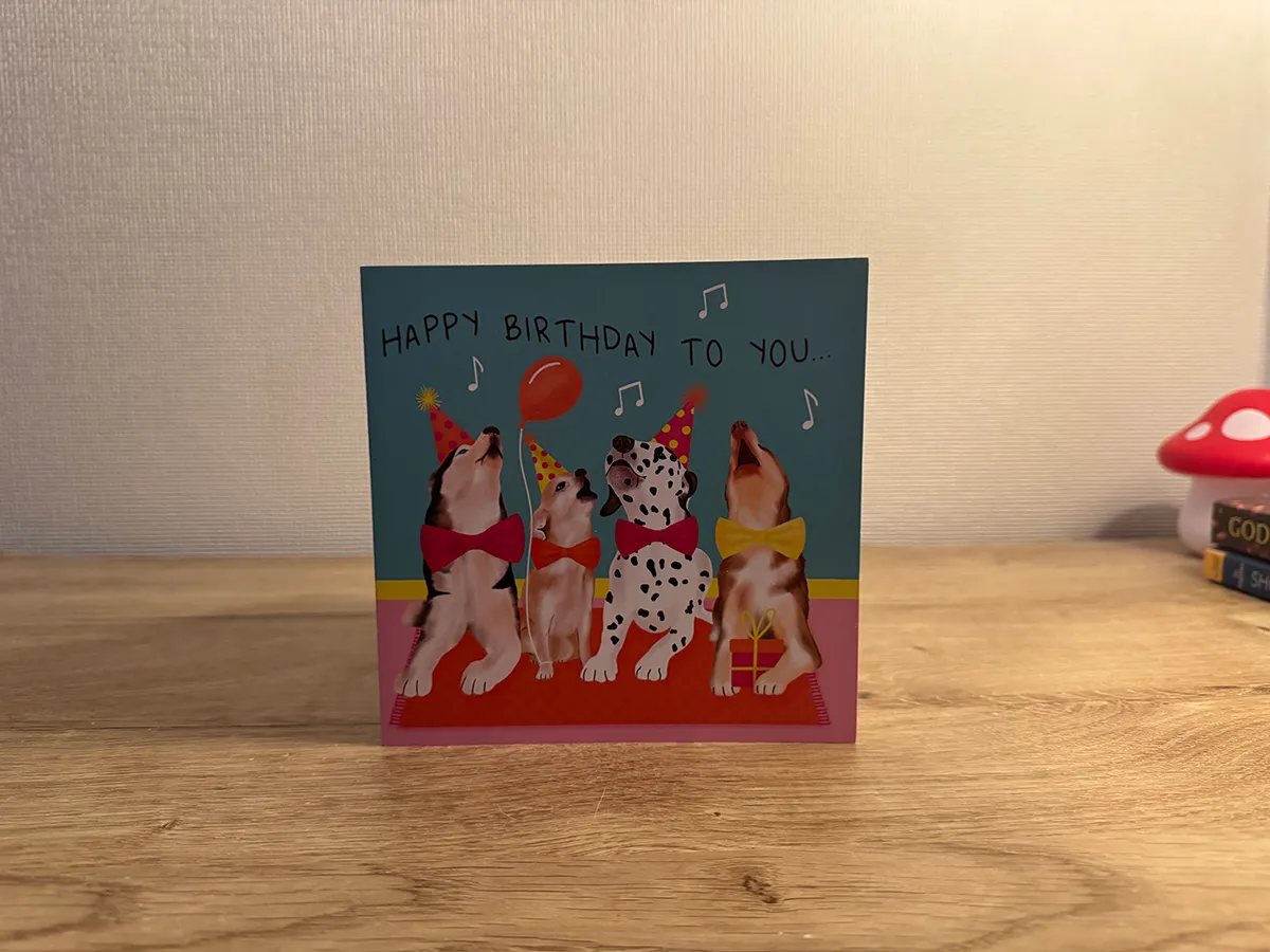 Alt: A birthday card placed on a dresser. The front of the card reads happy birthday to you with imagery of dogs