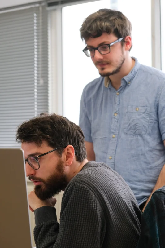 Two developers reviewing code together on a laptop screen