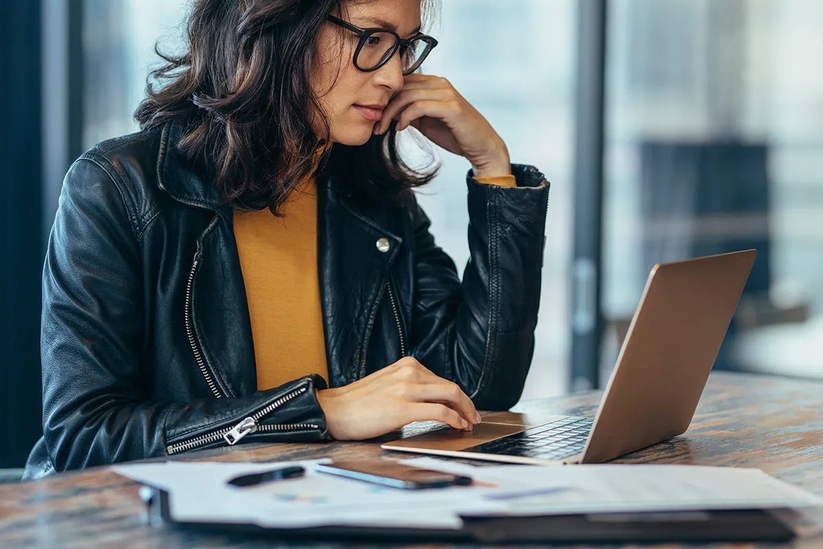 Woman working on a laptop at a desk with printed reports beside her