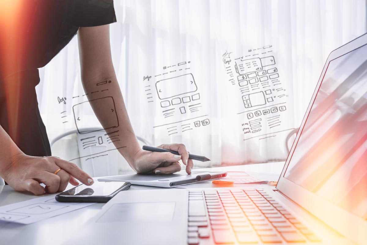 A female web designer leaning over a laptop overlayed with sketches of web pages