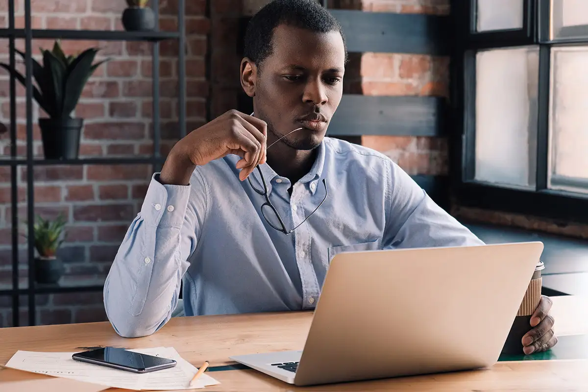 a man with a coffee looking at a laptop.