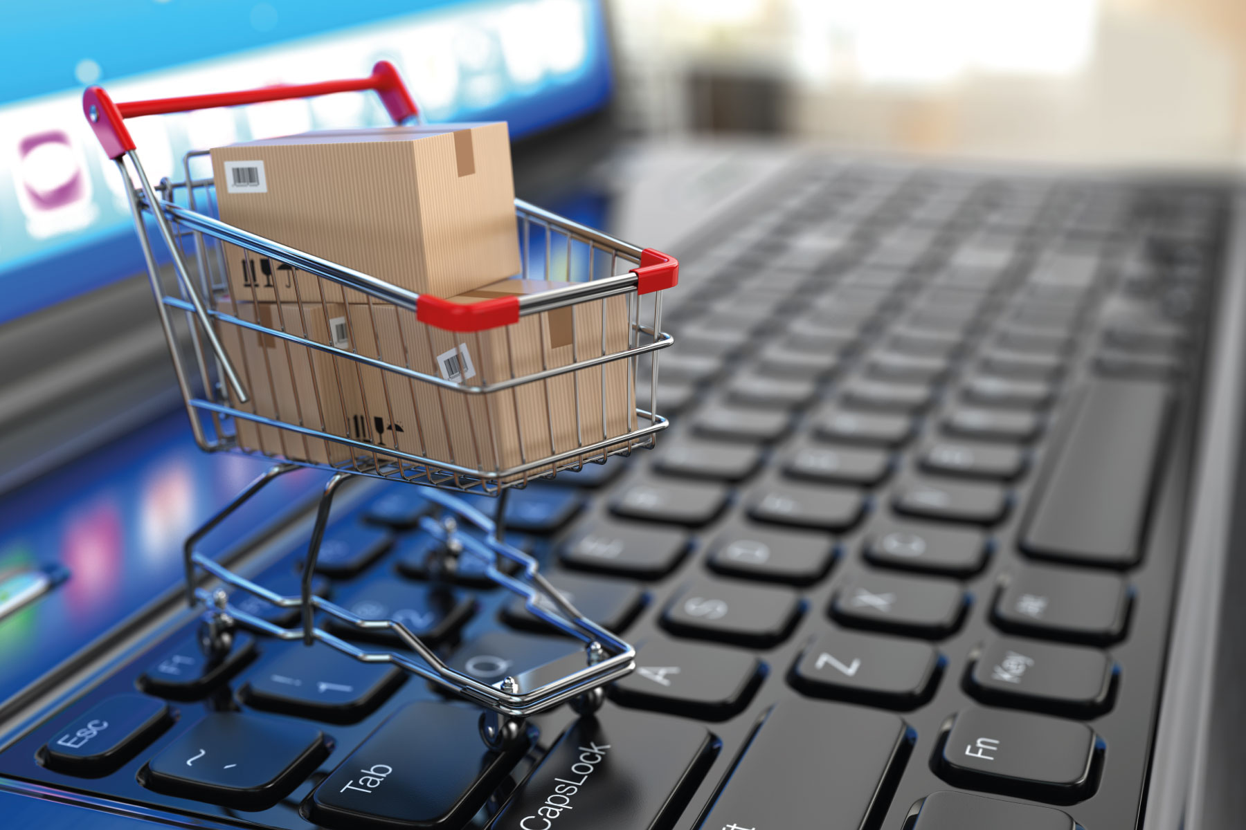 a shopping trolley with parcels in it on top of a laptop representing e-commerce