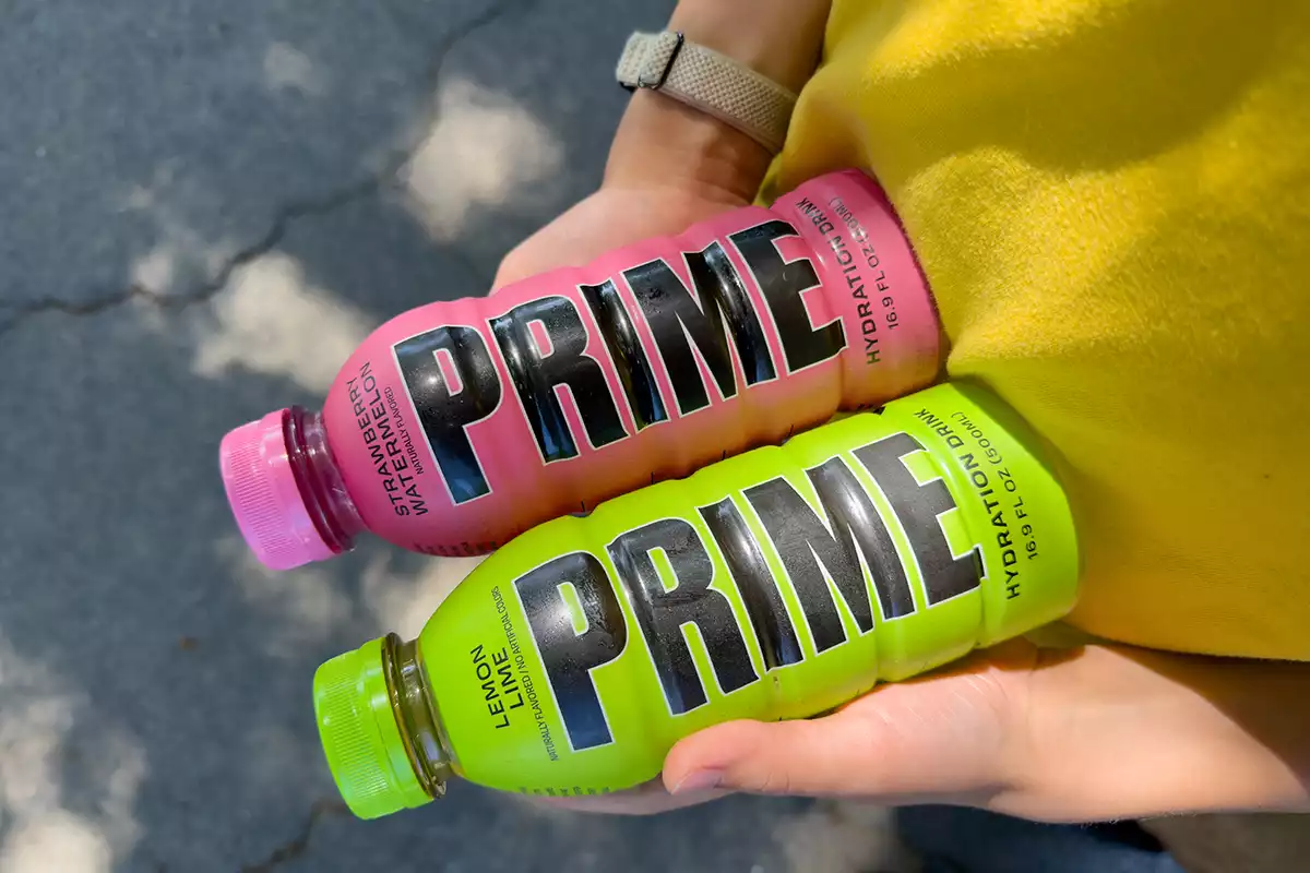 a person in a yellow top holding a pink and a green prime bottle