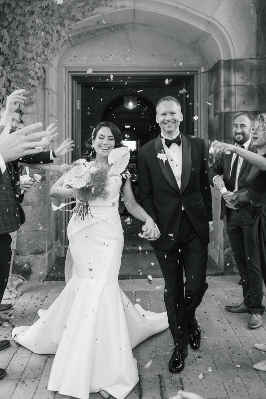 a bride and groom with confetti aftery getting married. the image is greyscaled.